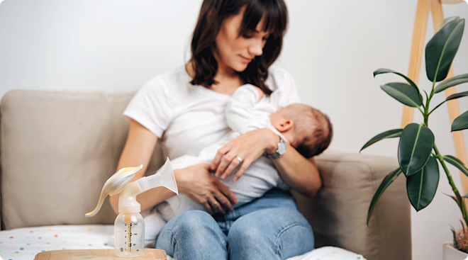 mom breastfeeding baby with breast pump on table nearby