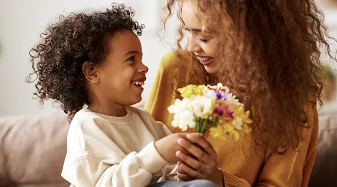 young boy smiling while giving his mother flowers