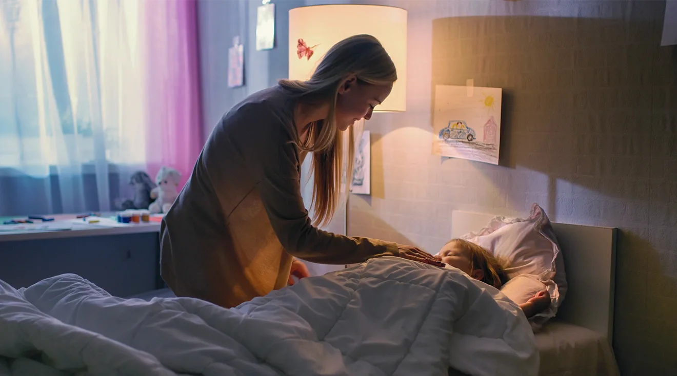 mother tucking child into bed at night