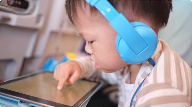 toddler wearing headphones playing on ipad on airplane