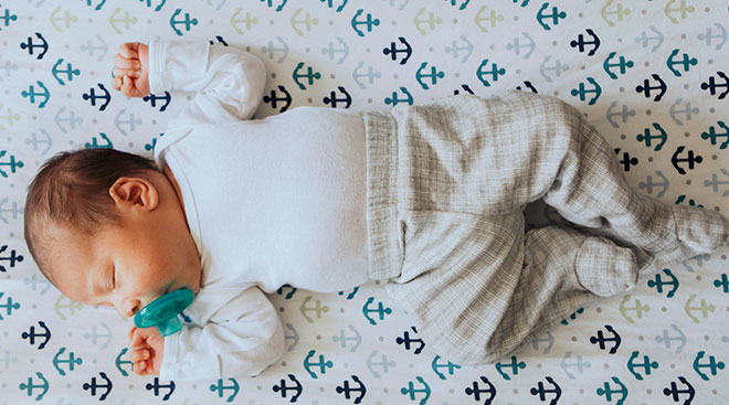 Newborn baby sleeping on its back on anchor pattern crib sheets,