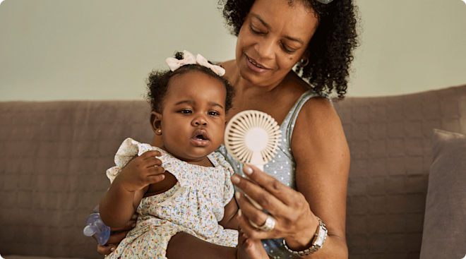 A grandmother holding a handheld fan with her granddaughter.