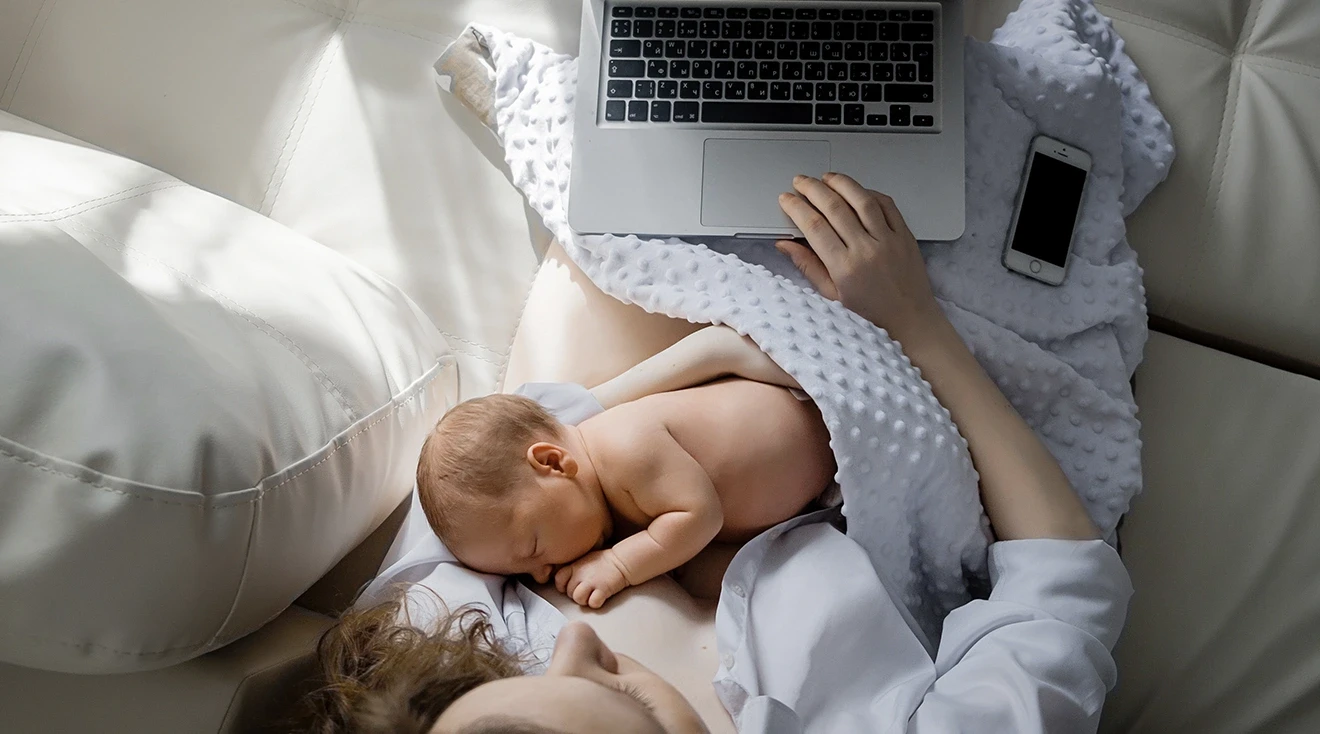mother breastfeeding baby while browsing on laptop