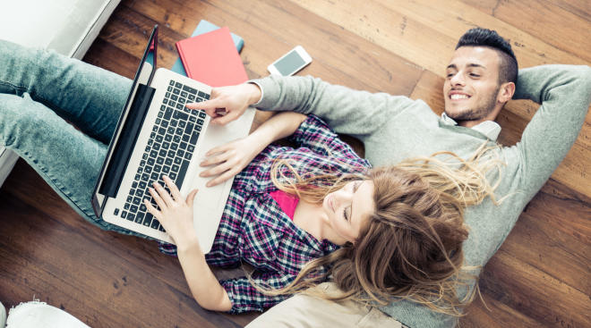Couple lying on the floor shopping on their laptop