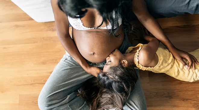 young girl lying with her pregnant mother and kissing her mom's belly