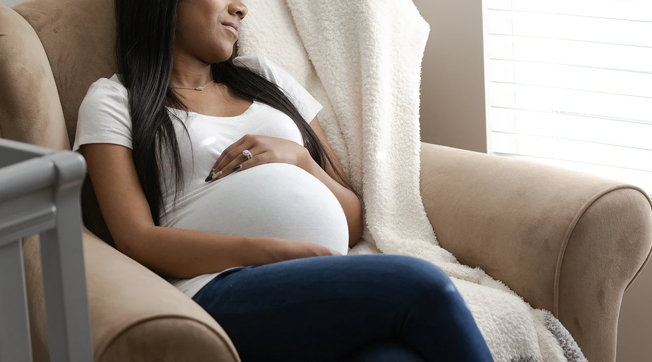 pregnant woman sleeping in chair next to baby crib at home