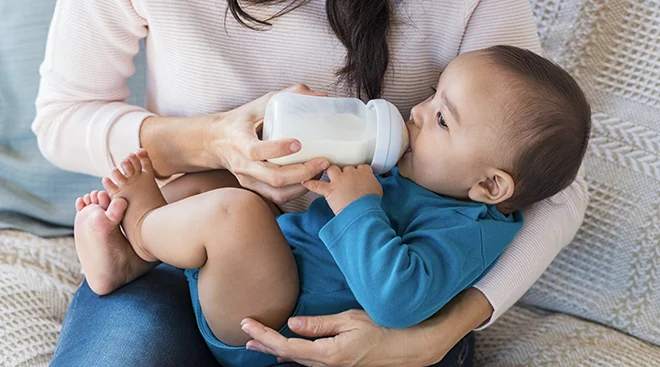 mother feeding baby a bottle at home