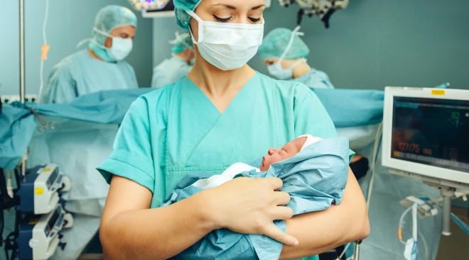nurse holding newborn baby in hospital delivery room after c-section.
