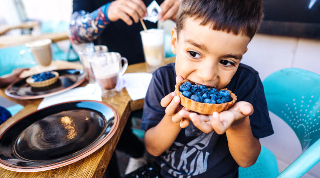 little boy at restaurant devouring blueberry tart dessert