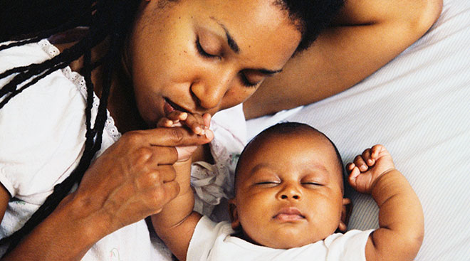 Black mother kisses her sleeping newborn's hand