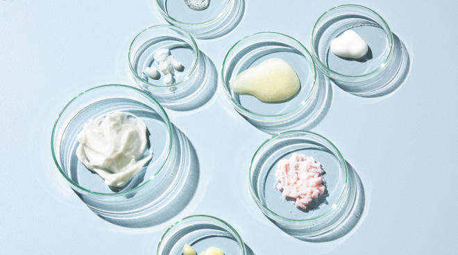Overhead of petri dishes artfully arranged each containing different skincare products. 