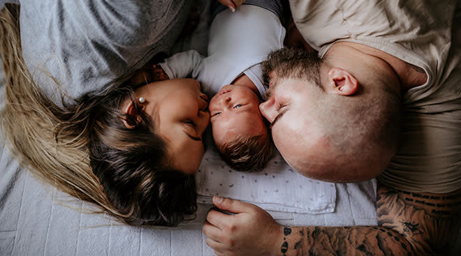 mother and father snuggling in bed with their newborn baby