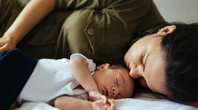 mother lying with newborn baby in bed at home