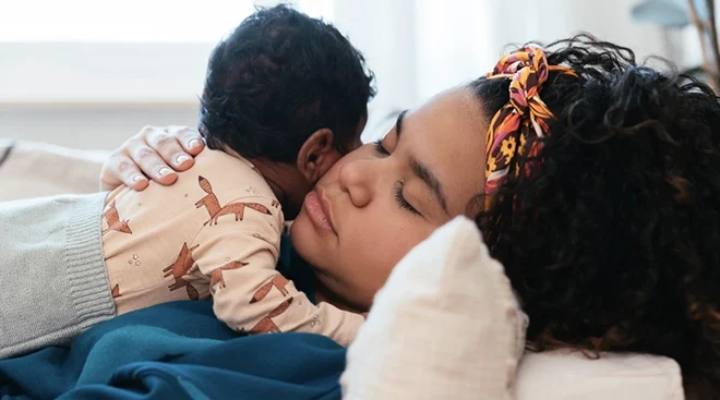 mother holding sleeping baby on sofa at home