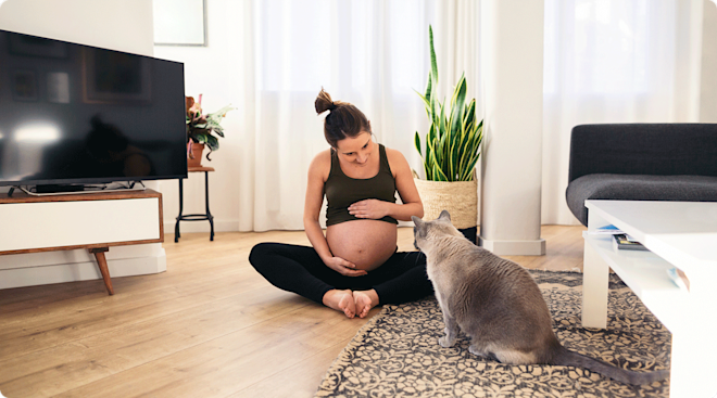 A pregnant woman sitting on the floor at home with her cat.