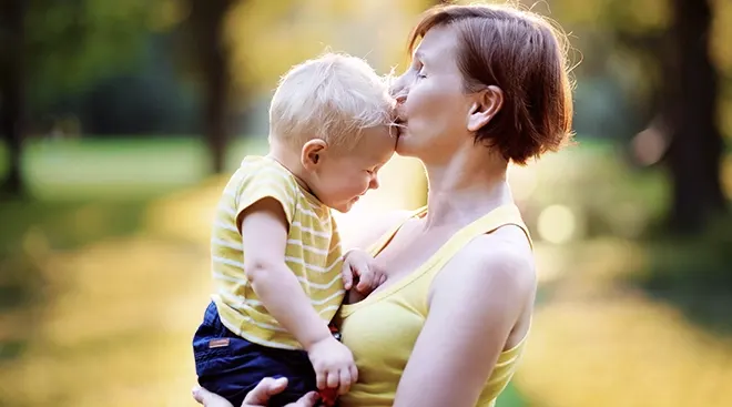 middle aged mother holding her toddler and kissing him on the forehead