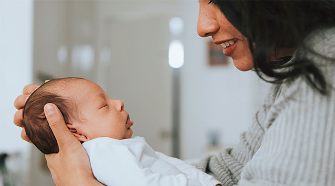 cropped smiling face of new mom looking at and holding her newborn baby