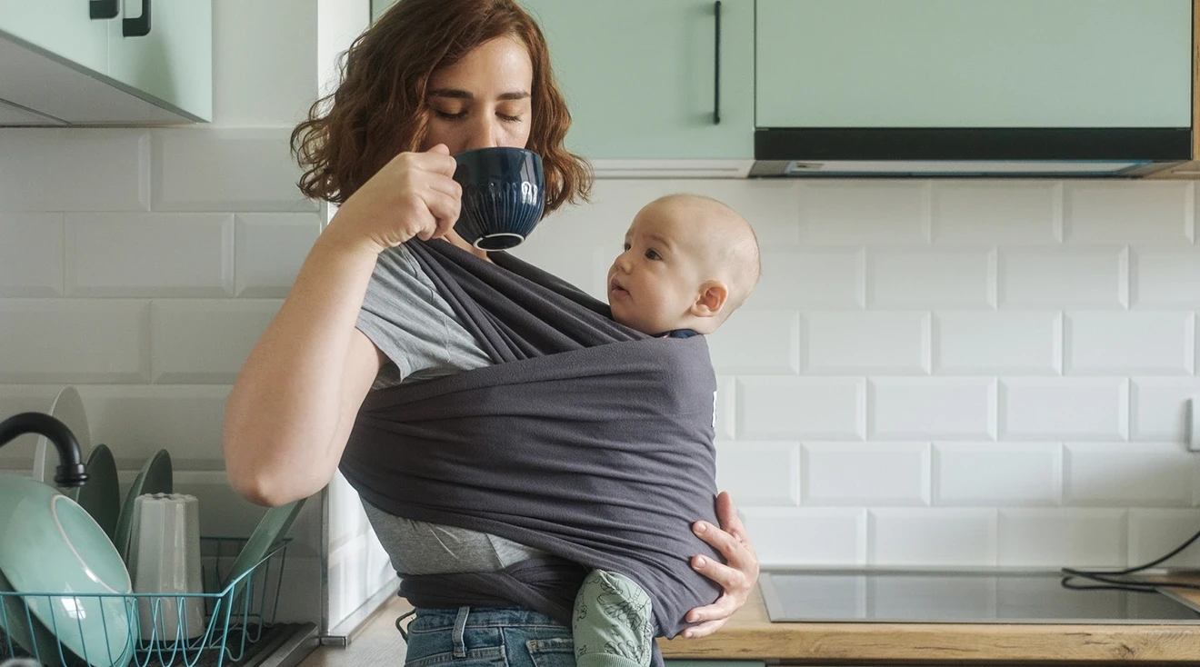 mom holding baby while drinking coffee in kitchen