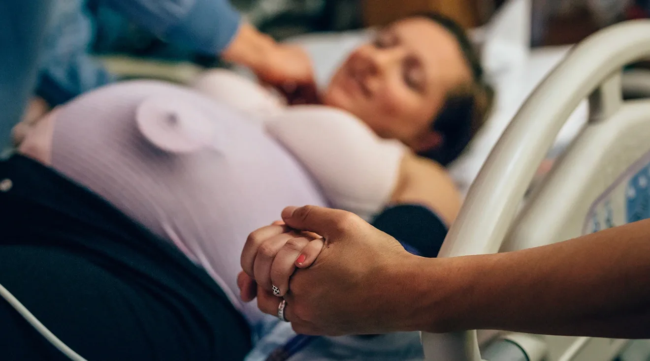 couple holding hands while woman is in labor in hospital bed