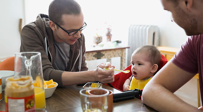 Dads feeding their baby, baby food at kitchen table.