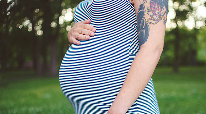 Pregnant woman with tattoos touching her belly. 
