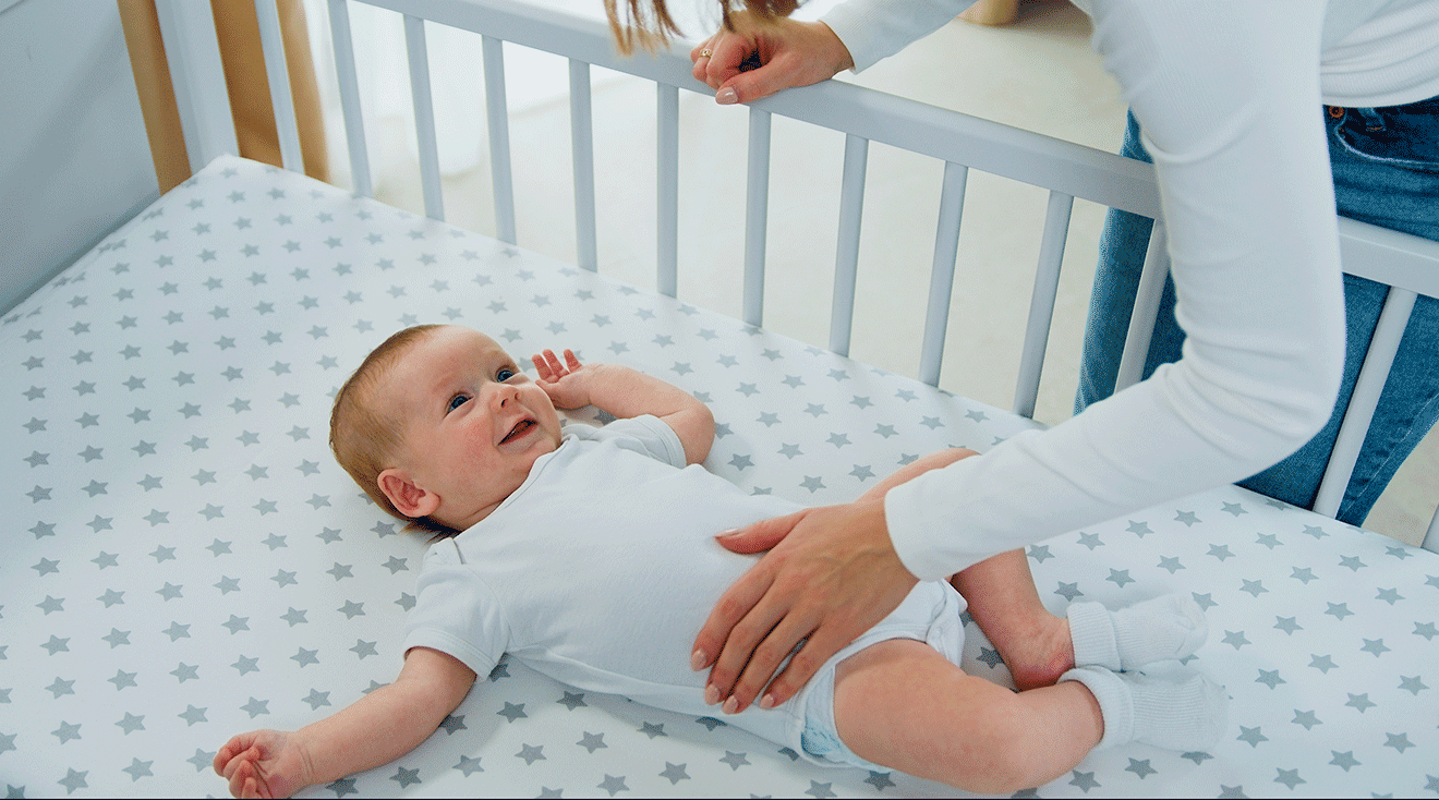 mother putting baby into bare crib for safe sleep