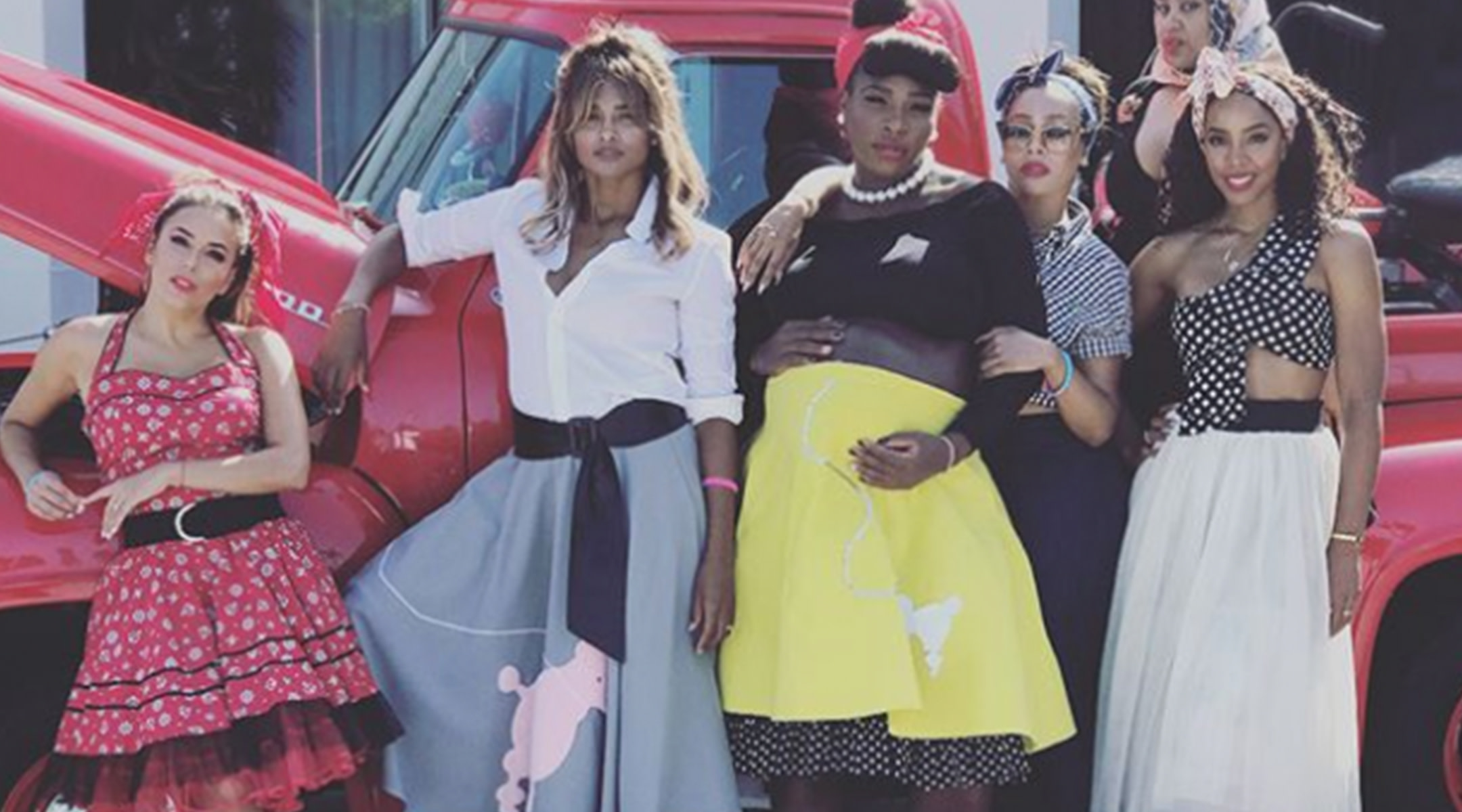 Serena Williams and celebrities posing in 1950s poodle skirts in front of a vintage red pickup truck at her baby shower
