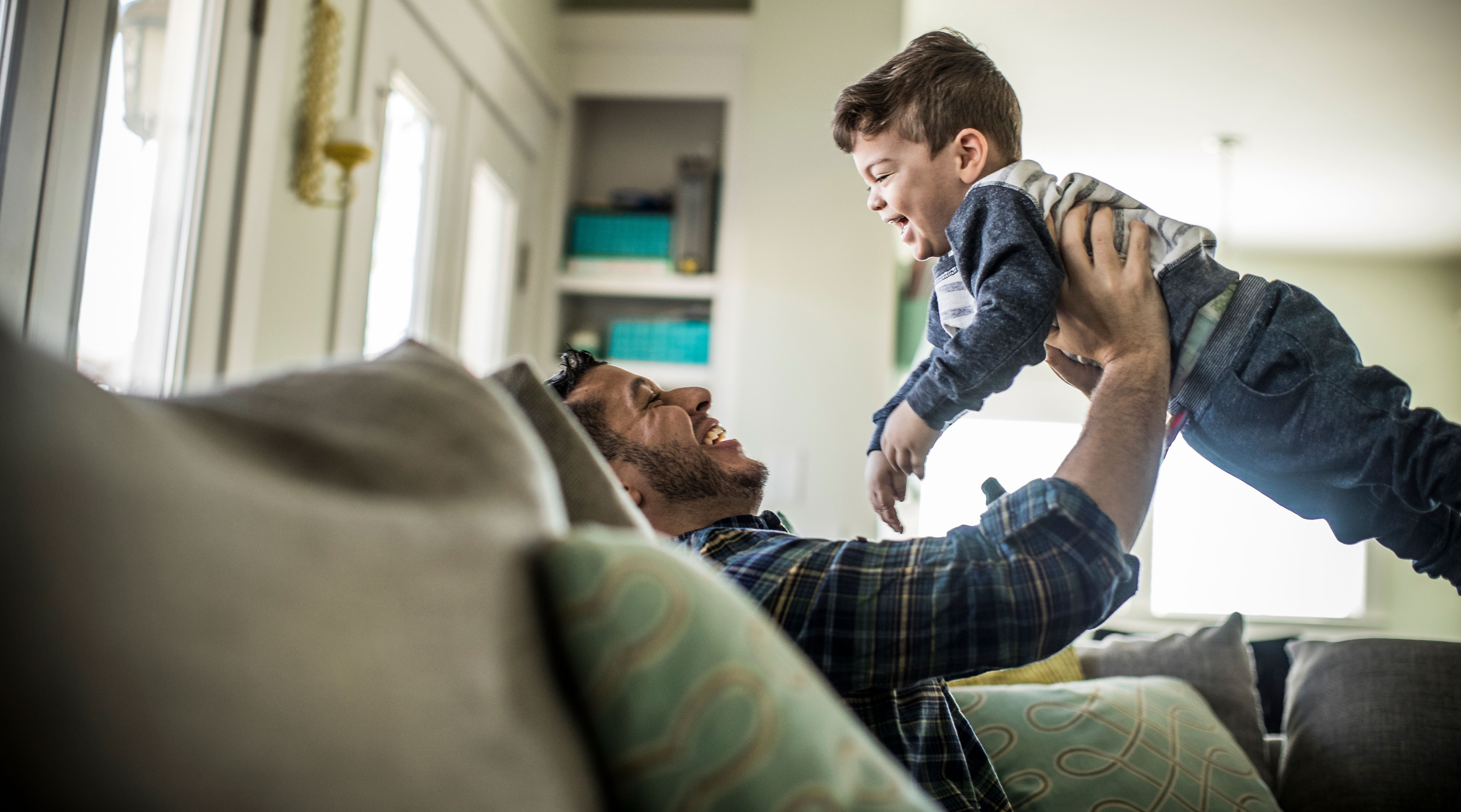 dad plays with laughing young son at home