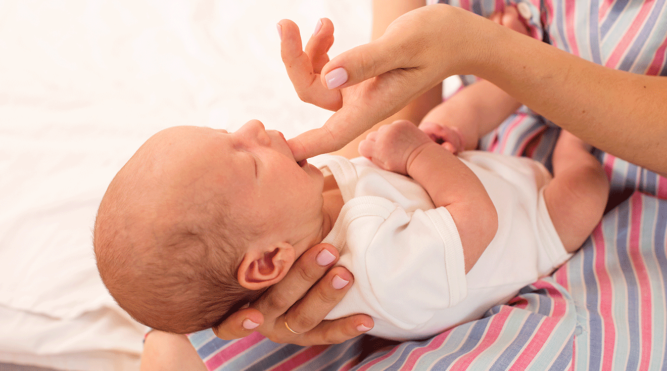 mom putting finger in newborn baby's mouth to test sucking reflex