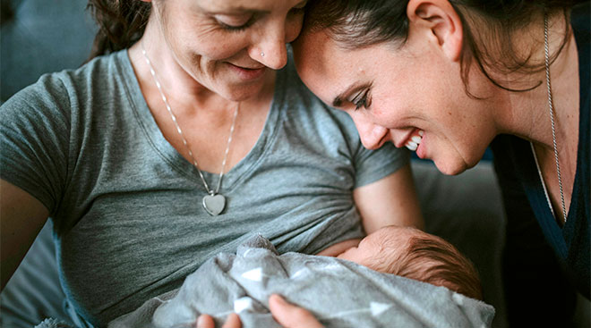 Mom breastfeeds her newborn baby with partner close-by. 