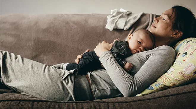 tired mother lying on couch with baby on chest