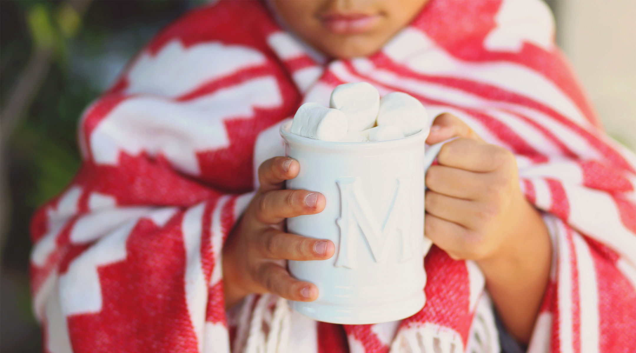 child wrapped in blanket drinking hot chocolate during winter time