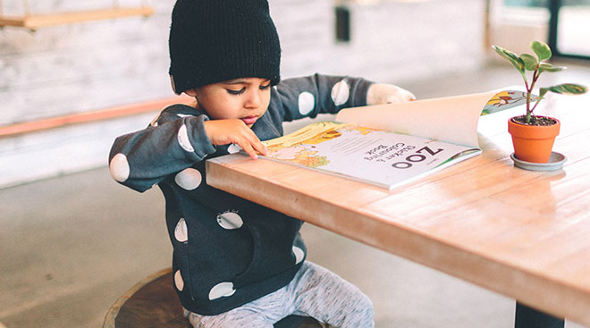 independent toddler reading a book at table