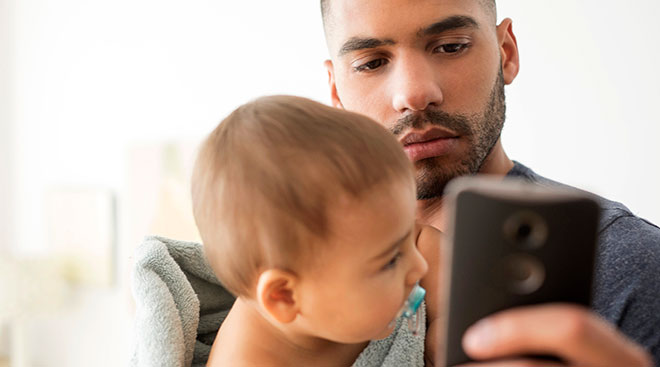 worried dad with baby checking his phone