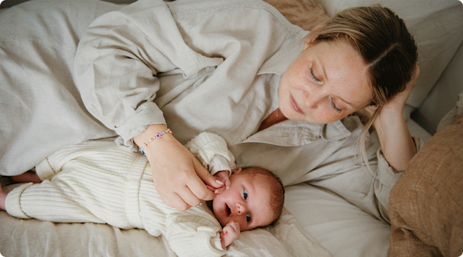 A postpartum mother lying with her newborn baby in bed at home.