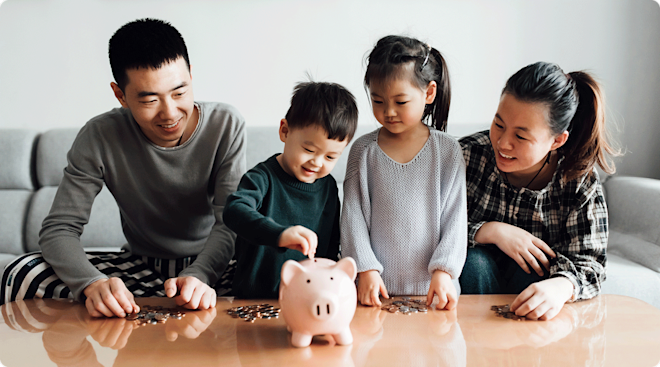 A family with two young children putting money into a piggy bank at home.