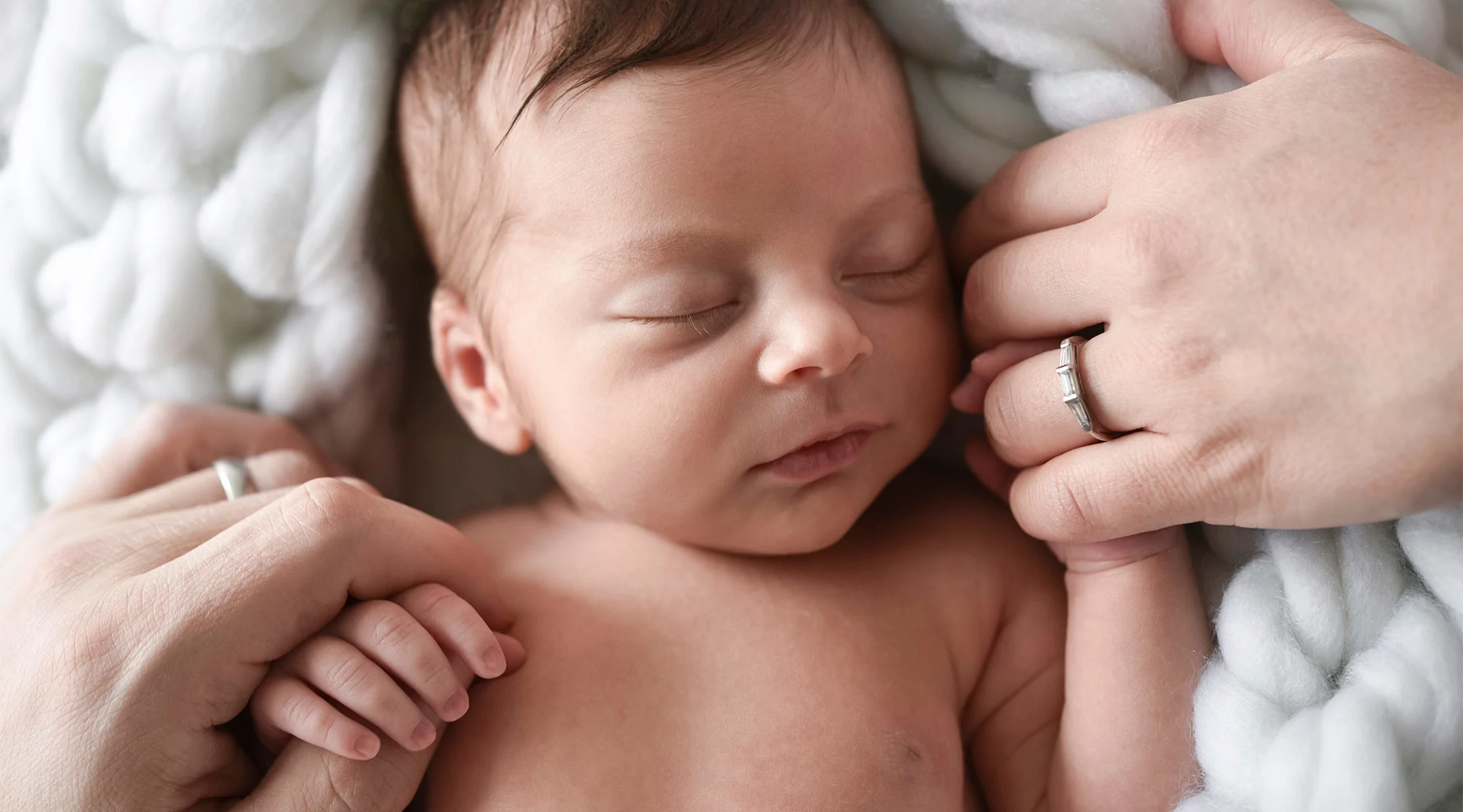 newborn baby holding hands with its parents