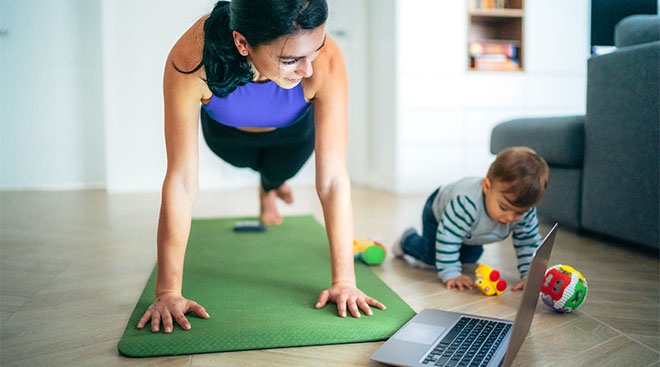 Mom exercises at home while her toddler who sits nearby refuses to nap. 