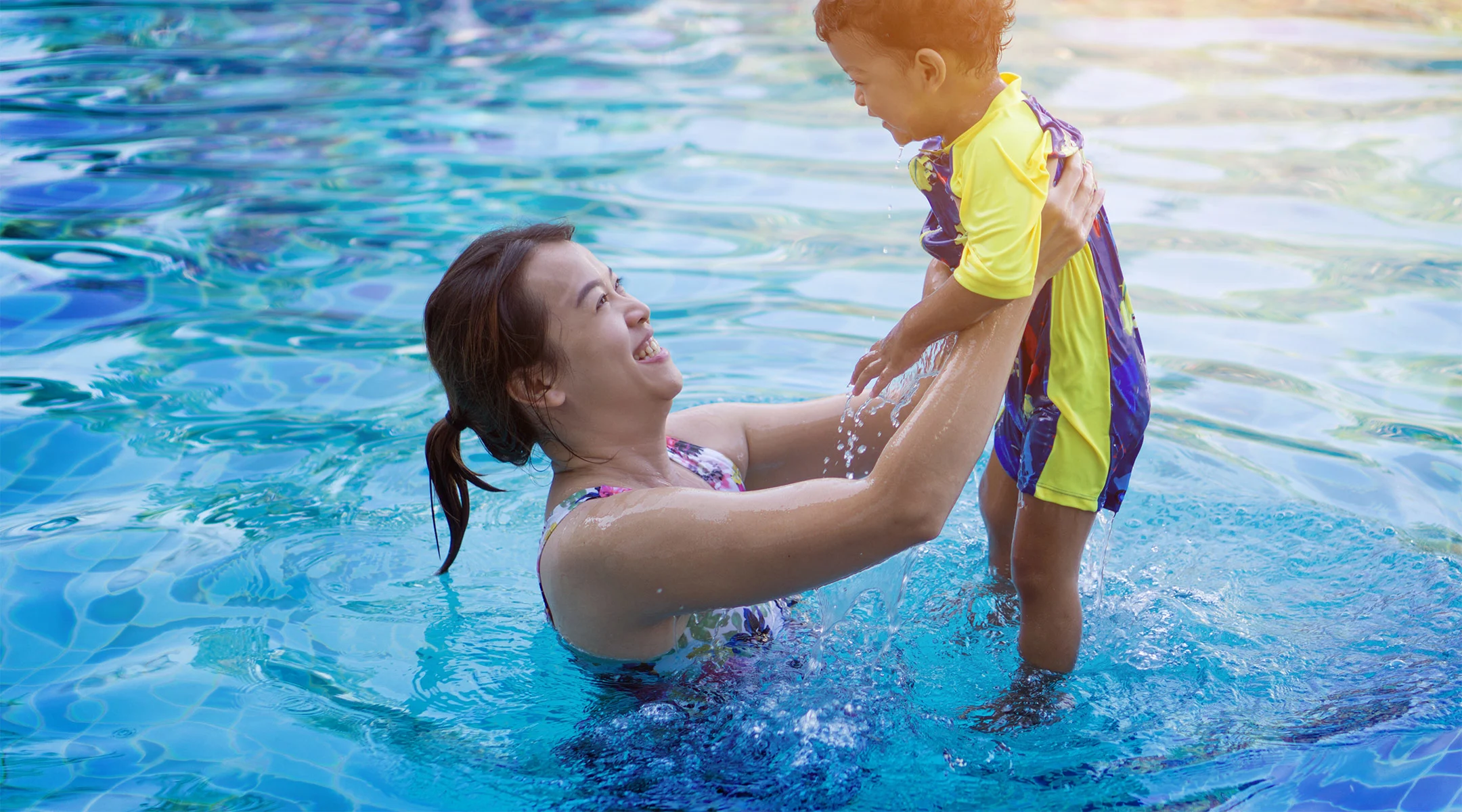 mom lifting up her young son in the pool
