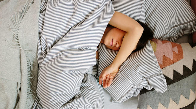 tired woman resting in bed with her arm over her face