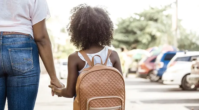 rear view of mother holding daughter's hand while walking into school