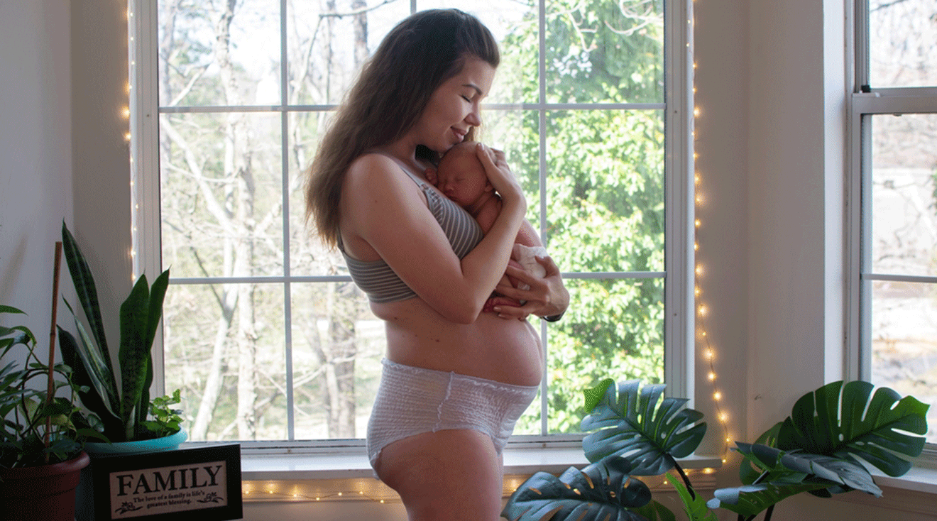 postpartum mother wearing a diaper and holding newborn baby at home