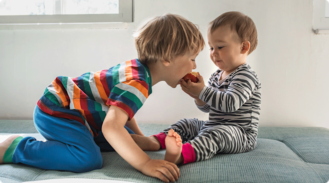 A happy toddler sharing an apple with their sibling at home.