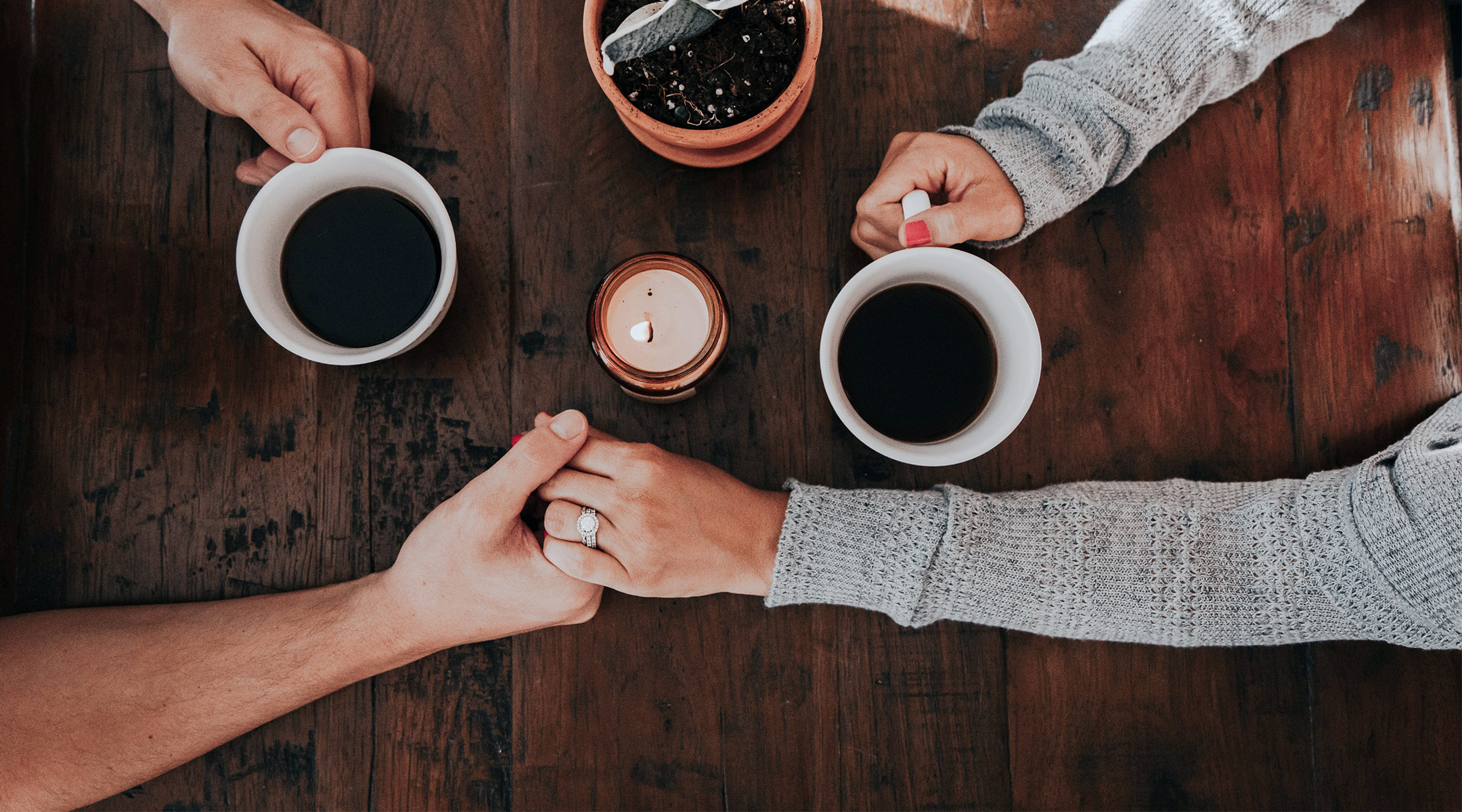 sad couple holding hands across table with coffee