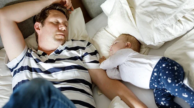 father and baby asleep in bed during the day