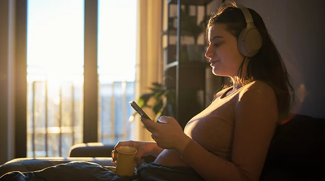 pregnant woman listening to a podcast at home while sitting on the couch
