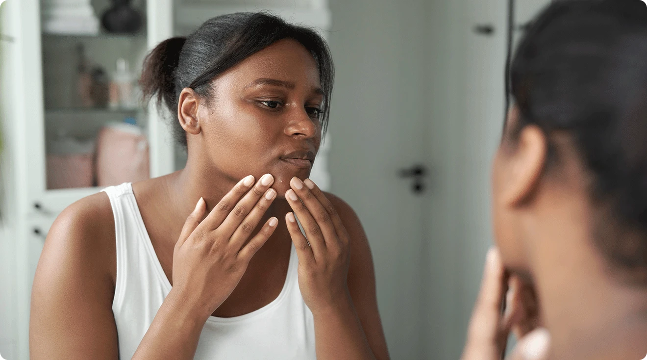 woman looking at acne in bathroom mirror