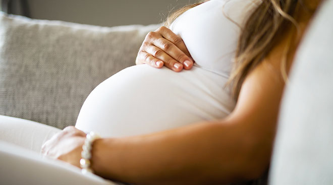 close up of woman's pregnant belly while sitting on couch at home
