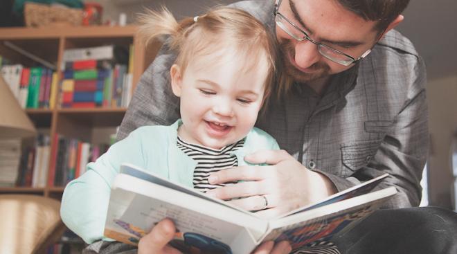 father holding toddler daughter with book