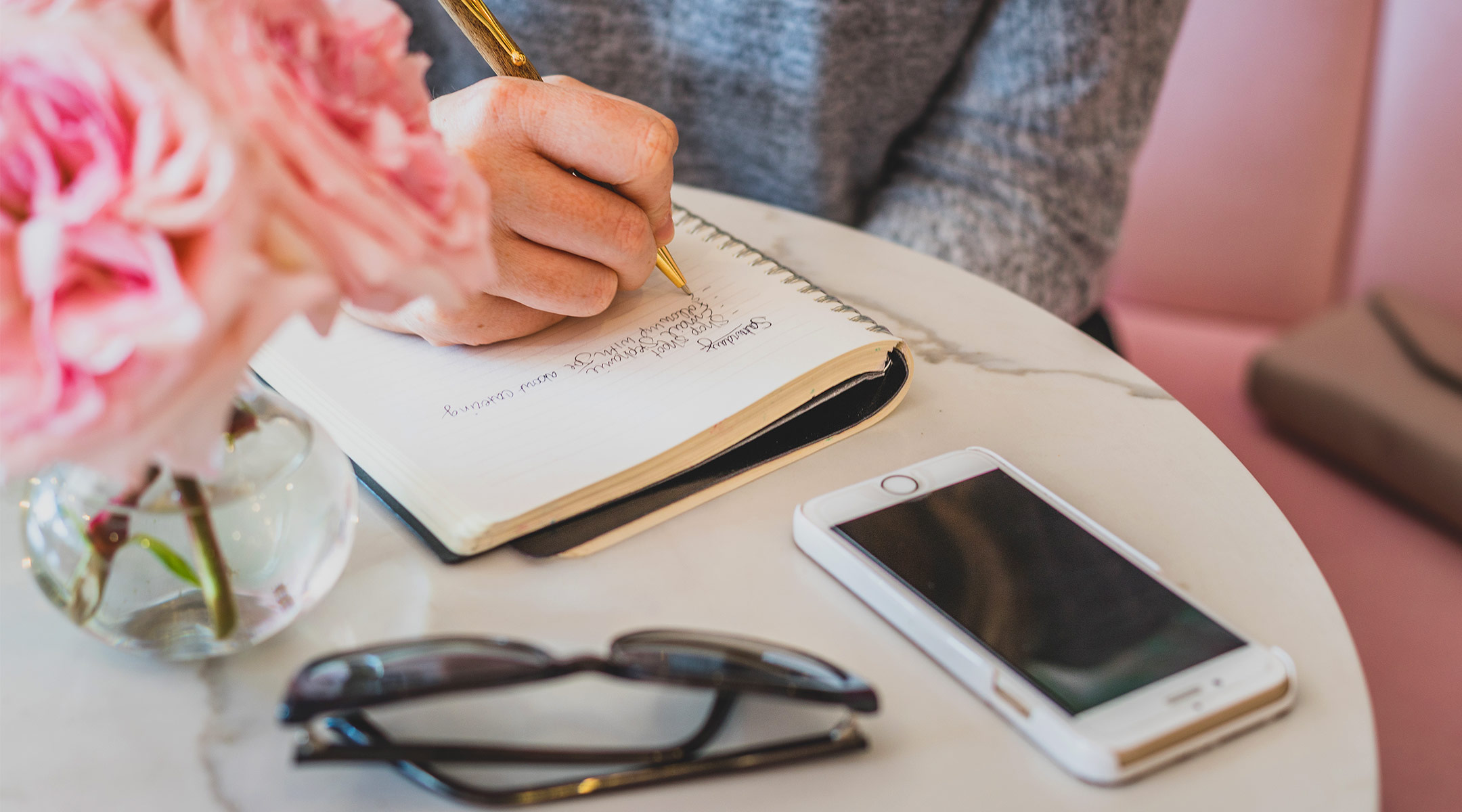 woman writing in notebook with her cell phone nearby